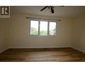 A room with a ceiling fan and a window with a view of trees and a building outside.