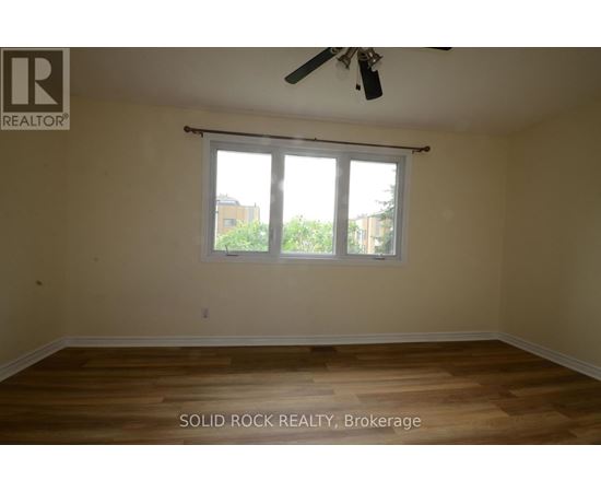 A room with a ceiling fan and a window with a view of trees and a building outside.