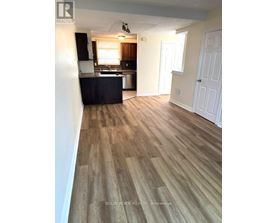 A room with wooden flooring and a kitchen area in the background.