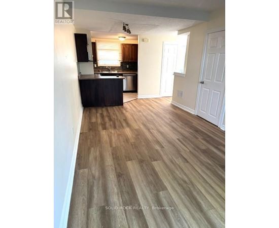 A room with wooden flooring and a kitchen area in the background.