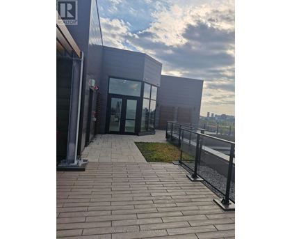 The image shows a modern building entrance with glass doors and a brick walkway leading to it.