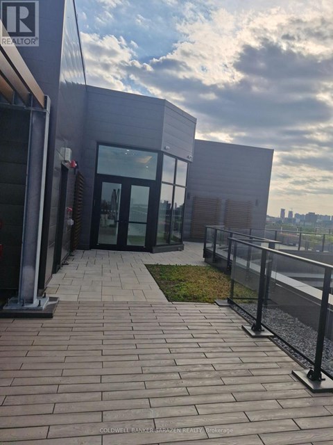 The image shows a modern building entrance with glass doors and a brick walkway leading to it.
