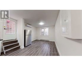 A spacious room with wooden flooring, a staircase, and a refrigerator.