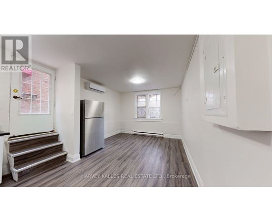 A spacious room with wooden flooring, a staircase, and a refrigerator.