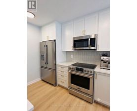 A kitchen with a stainless steel refrigerator, microwave, oven, and white cabinets.