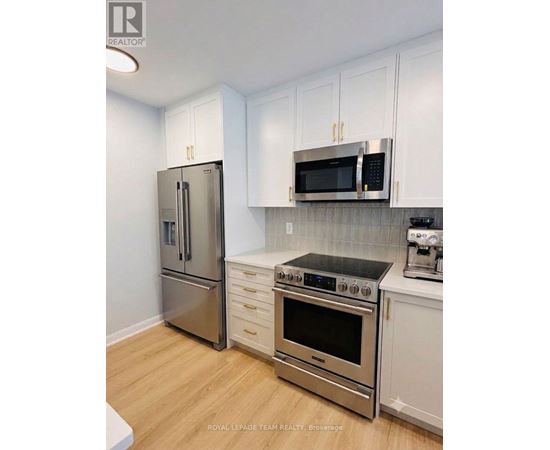 A kitchen with a stainless steel refrigerator, microwave, oven, and white cabinets.