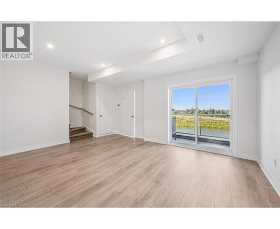A spacious room with wooden flooring and a large window overlooking a grassy area.