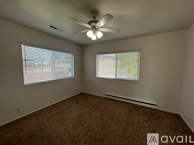 A room with a carpeted floor, a ceiling fan, and two windows with blinds.