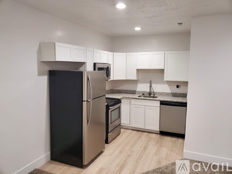 A kitchen with a black fridge, stainless steel oven and white cabinets.