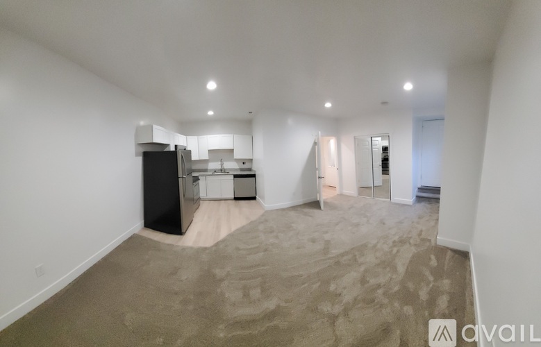 A spacious empty room with a kitchenette in the background.