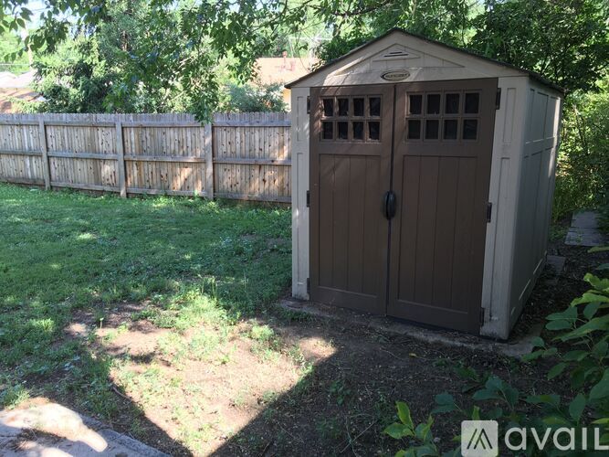 A brown shed with a brown door and windows is in a grassy area.