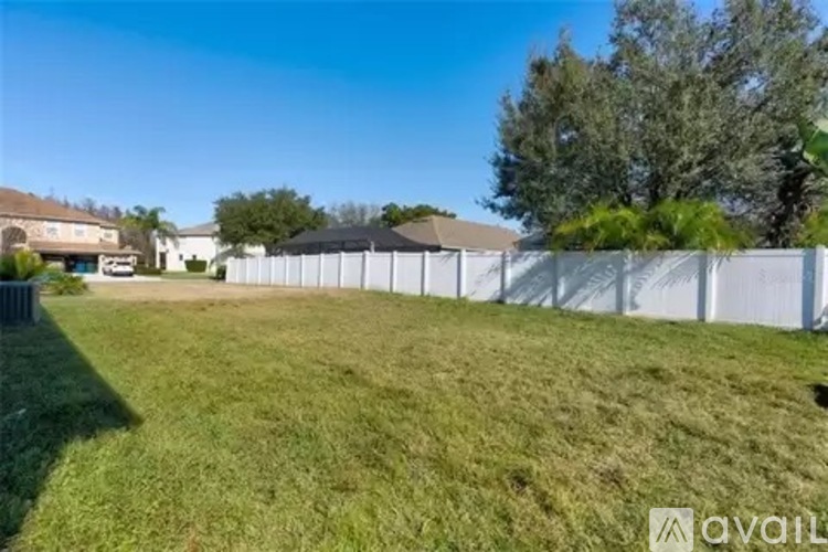 A grassy area with a white fence and trees in the background.