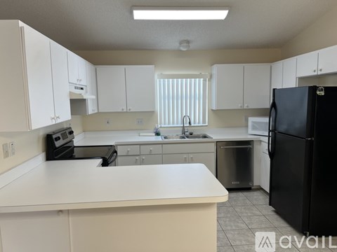 A kitchen with white cabinets and a black refrigerator.