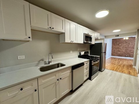 A kitchen with white cabinets and appliances, a sink, and a brick wall in the background.