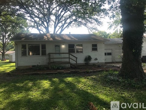 A small white house with a porch and a tree in front.