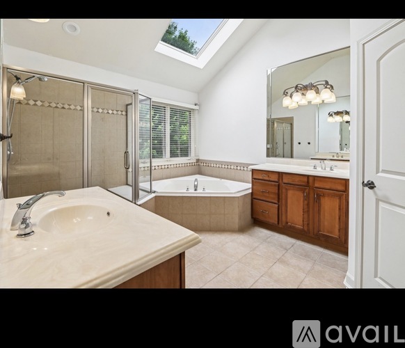 A bathroom with a skylight, a tub, a sink, and a mirror.