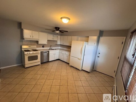 A kitchen with white appliances and cabinets, a ceiling fan, and a tiled floor.