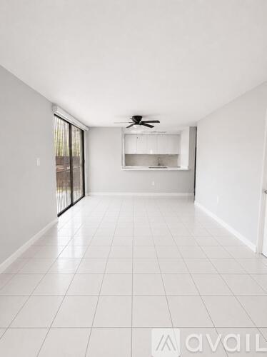 A spacious room with a ceiling fan and a kitchenette in the background.