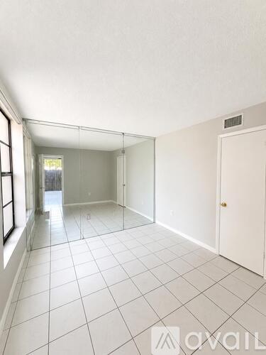 A spacious room with white tiled flooring and a large window on the left.