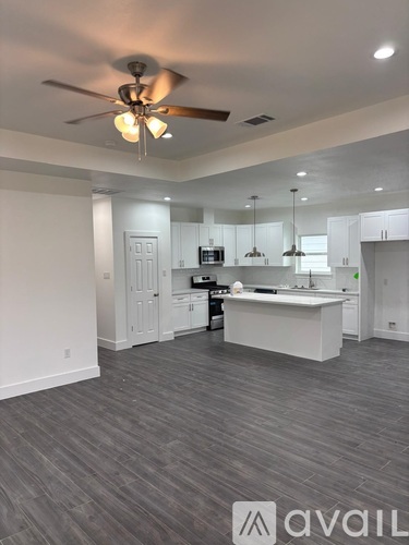 A spacious kitchen and living room with a ceiling fan and grey flooring.