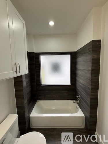 A bathroom with a white toilet, a white bathtub, and a window.