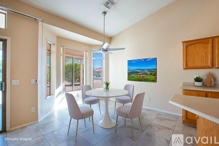 A dining room with a white table and chairs, a ceiling fan, and a painting of a landscape on the wall.