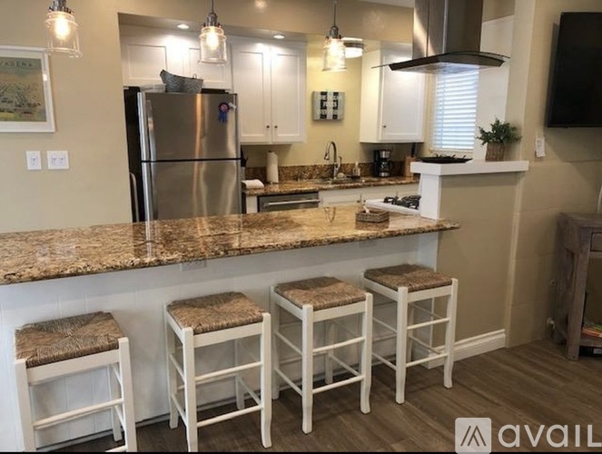 A kitchen with a granite countertop and white bar stools.