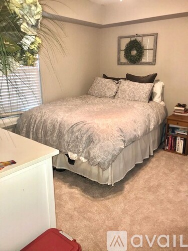 A bedroom with a bed, a wreath on the wall, and a plant in the corner.