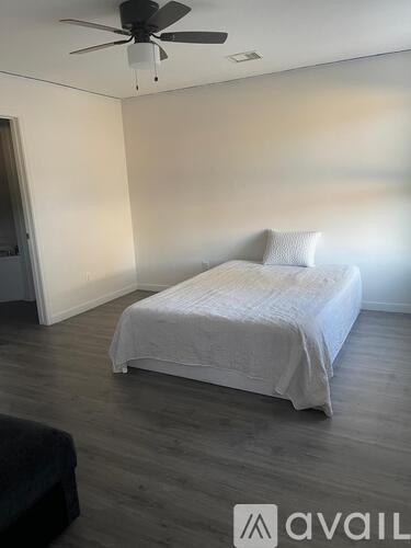 A bedroom with a bed, a ceiling fan, and a black ottoman.