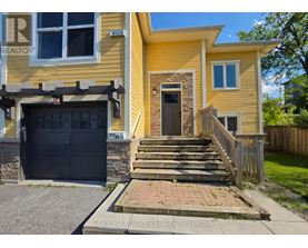 A yellow house with a black garage door and a stone pillar in front of the door.