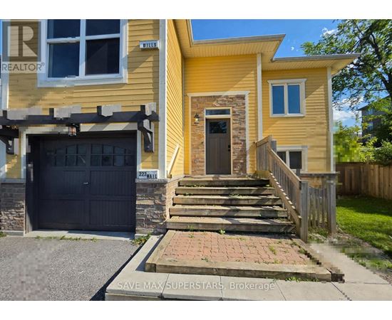 A yellow house with a black garage door and a stone pillar in front of the door.