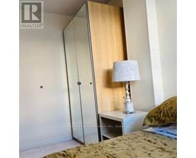 A bedroom with a bed, a nightstand with a lamp, and a wardrobe.
