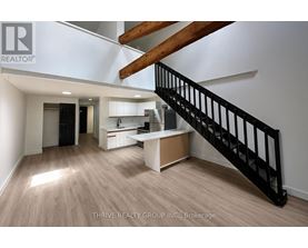 A spacious room with a staircase and a kitchen area.
