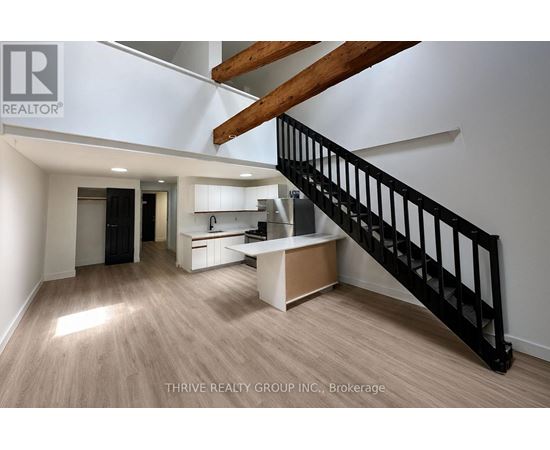 A spacious room with a staircase and a kitchen area.