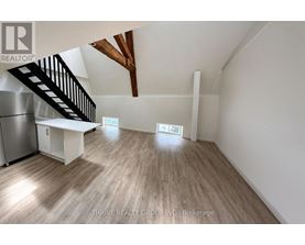 A spacious room with wooden flooring and a staircase leading to the upper level.