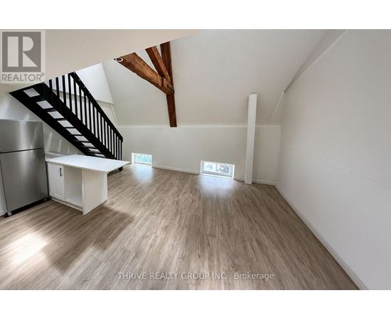 A spacious room with wooden flooring and a staircase leading to the upper level.