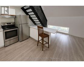 A kitchen with a stainless steel refrigerator, oven, and a wooden chair.