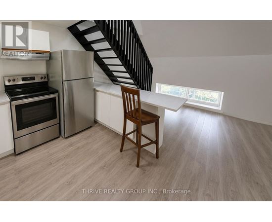 A kitchen with a stainless steel refrigerator, oven, and a wooden chair.
