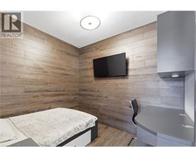 A bedroom with a bed, chair, and a television on the wall.