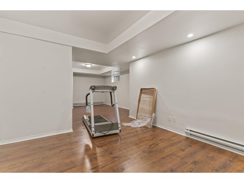 A room with a wooden floor and a white wall with a ladder and a wooden plank leaning against the wall.