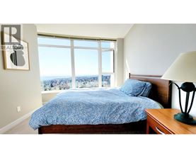 A bedroom with a bed, a lamp, and a window overlooking a cityscape.