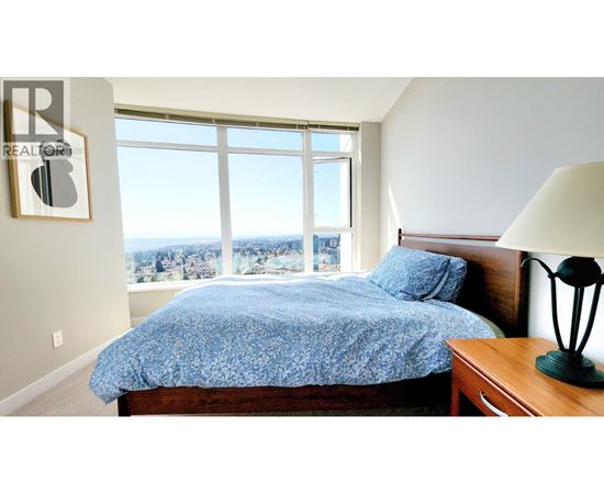A bedroom with a bed, a lamp, and a window overlooking a cityscape.