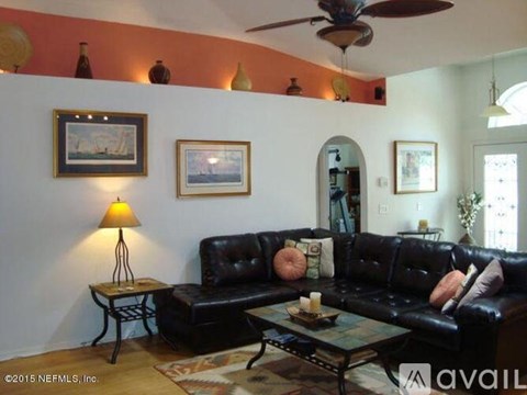 A living room with a black couch and a table with a candle on it.