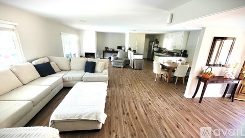A spacious living room with white furniture and wooden flooring.