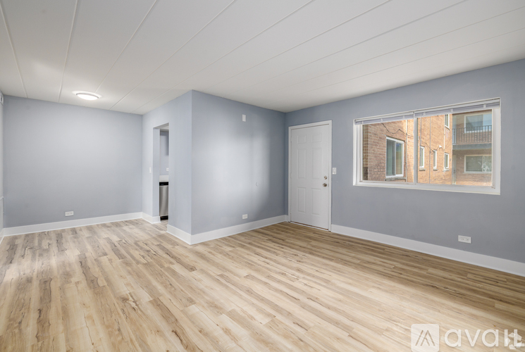 A spacious room with wooden flooring and a window showing an apartment building outside.