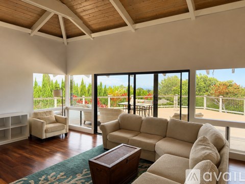 A living room with a couch, chairs, and a coffee table with a view of trees and a fence outside.