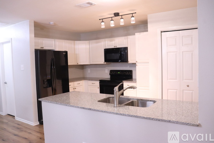 A kitchen with a black refrigerator, black microwave, and a granite countertop.