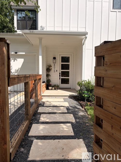 A white house with a wooden fence and a gravel pathway leading to the entrance.