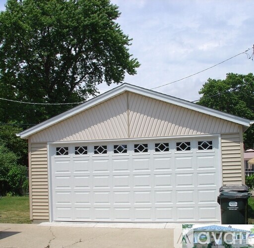 A white garage door is on a garage with a brown siding.