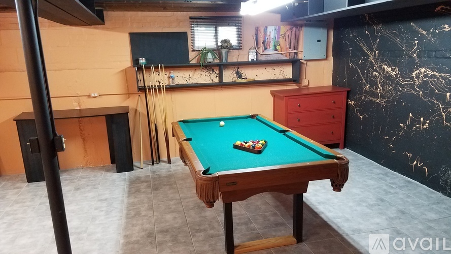A pool table with a green felt cloth and a red pool cue stand on it.